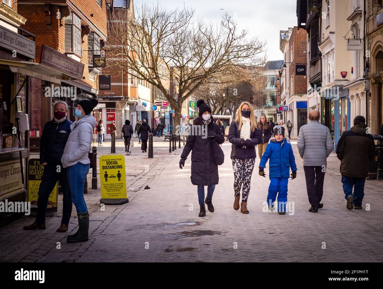 Verschiedene Menschen auf der Canterbury High Street tragen Masken und soziale Distanzierung an einem kalten Wintertag. Stockfoto