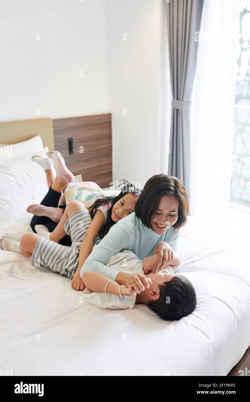 Vietnamesische Frau und ihre beiden Kinder umarmen und spielen an Bett nach dem Aufwachen Stockfoto