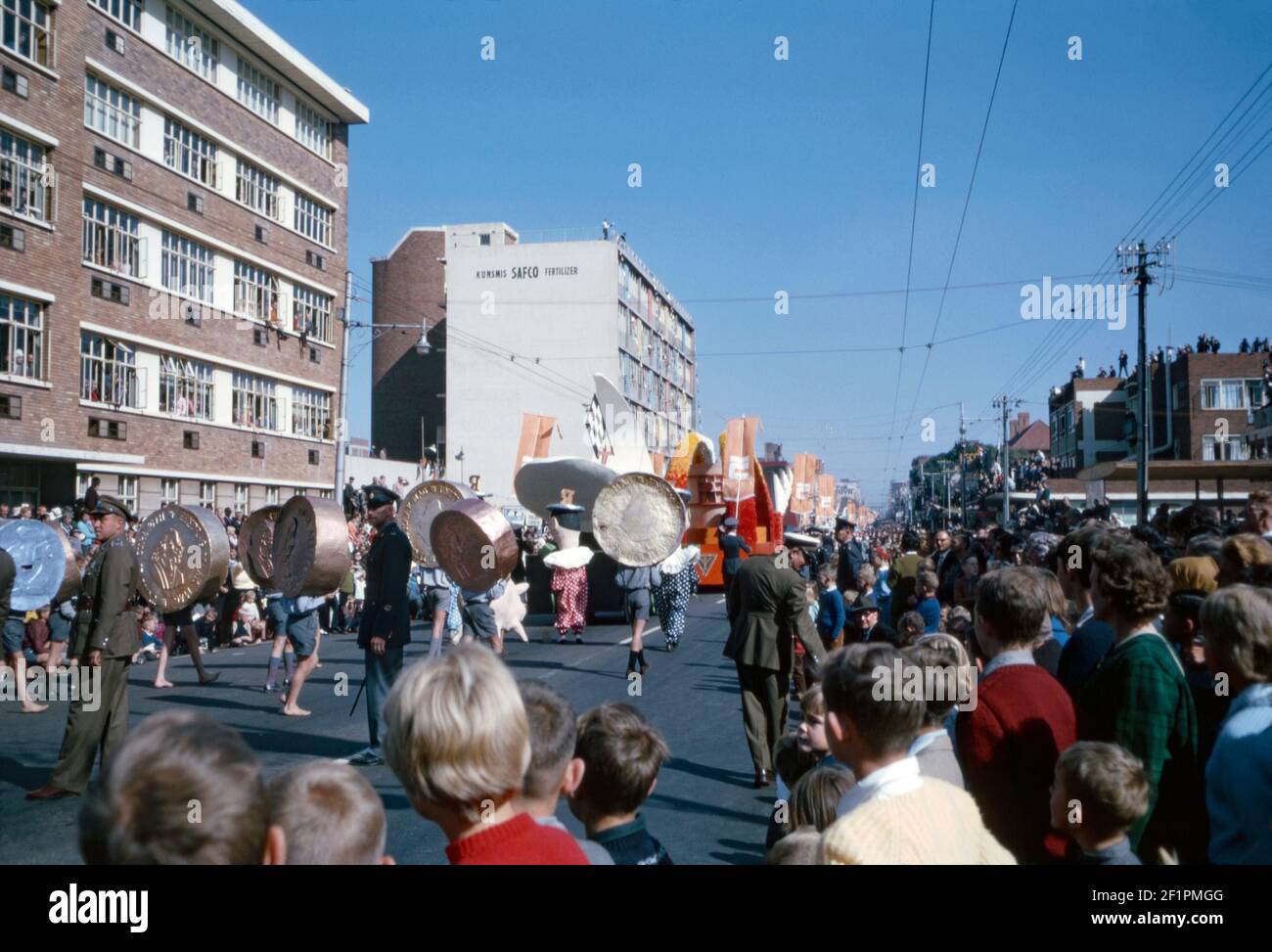 Eine Parade während der Apartheid-Ära, Durban, Südafrika, 1966. Dort tragen Kinder amüsante, riesige Kupfer-, Gold- und Silbermünzen ‘auf ihren Köpfen. Es ist sehr viel ein weißes Publikum Betrachten dieses Ereignis. Dieses Bild ist von einem alten Amateur 35mm Kodak Farbtransparenz. Stockfoto