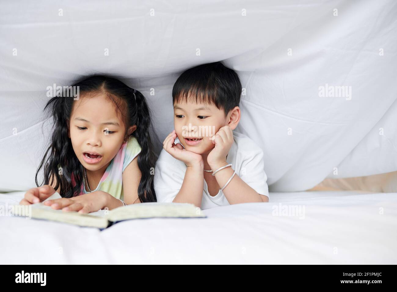Kleiner vietnamesischer Bruder und Schwester liegen unter der Decke und lesen Ein Buch Stockfoto