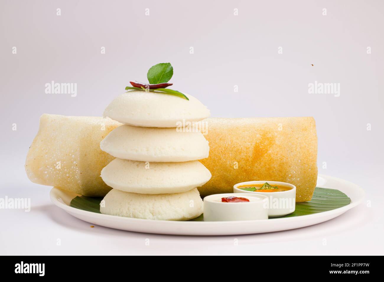 Ghee Roast Dosa und Idlii, südindisches Hauptfrühstück, das wunderschön auf einem weißen Teller mit Bananenblatt und Curry als Samba angeordnet ist Stockfoto