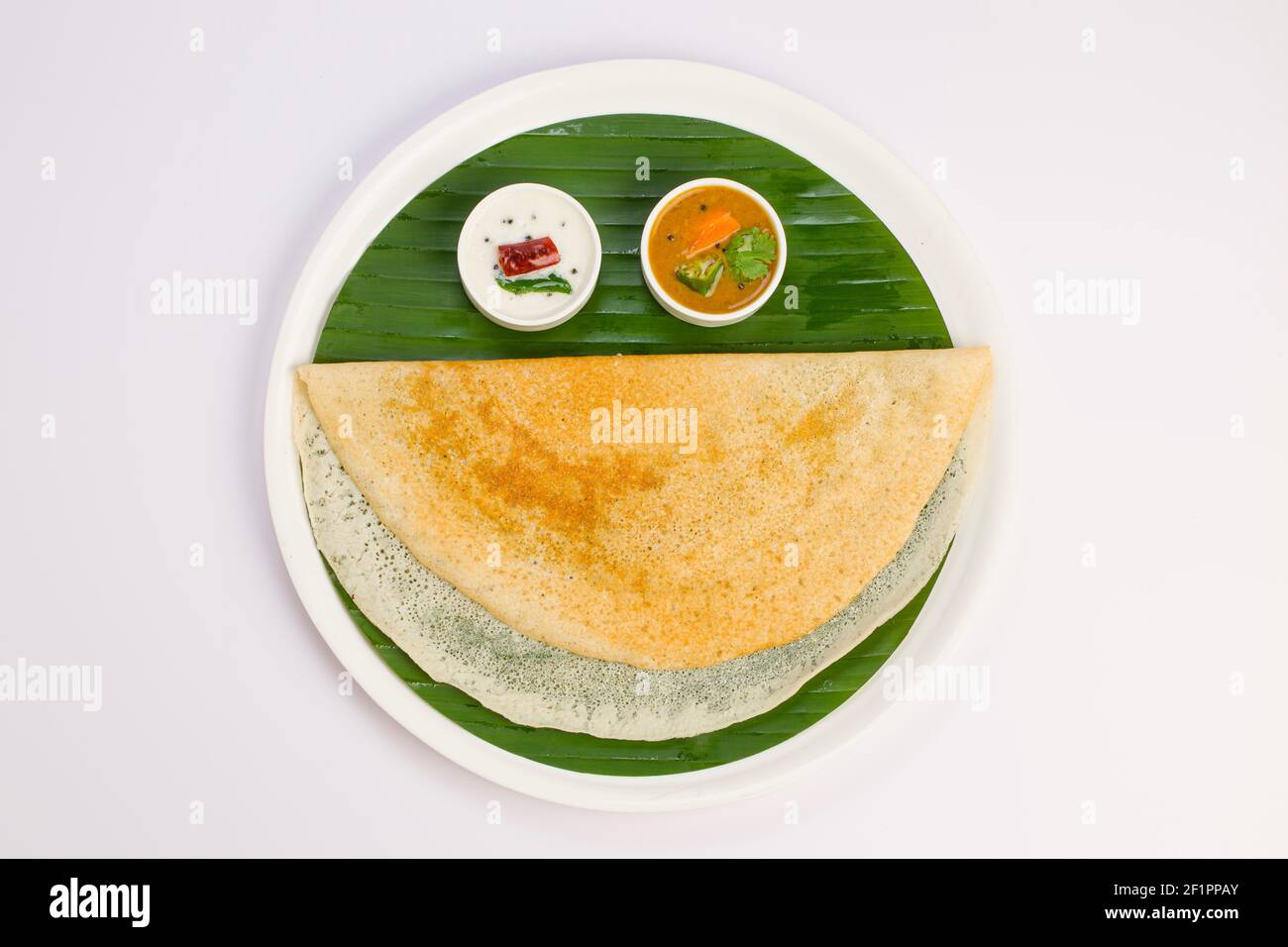 Ghee Roasted Dosa, südindisches Hauptfrühstück, das wunderschön wie ein lächelndes Gesicht auf einem weißen Teller mit Bananenblatt angeordnet ist. Stockfoto