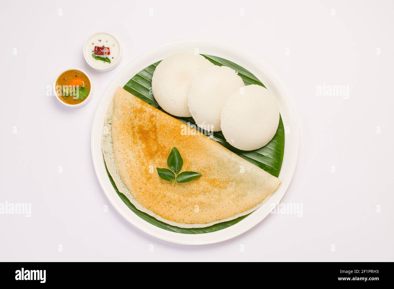 Ghee Roast Dosa und Idlii, südindisches Hauptfrühstück, das wunderschön auf einem weißen Teller mit Bananenblatt und Curry als Samba angeordnet ist Stockfoto