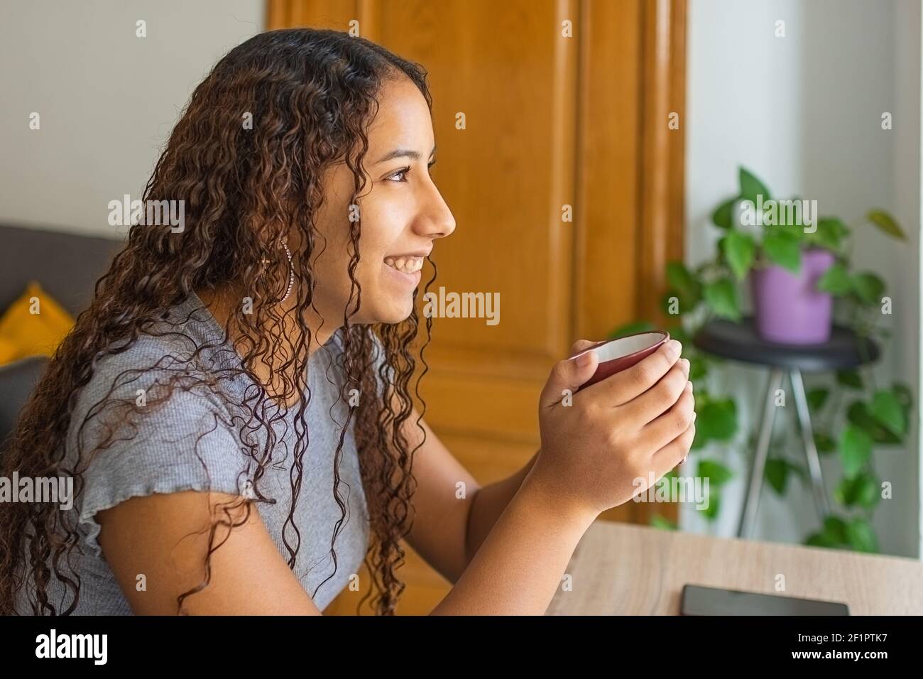 Lächelndes Mädchen, das am Tisch sitzt und eine Tasse Kaffee trinkt. Stockfoto