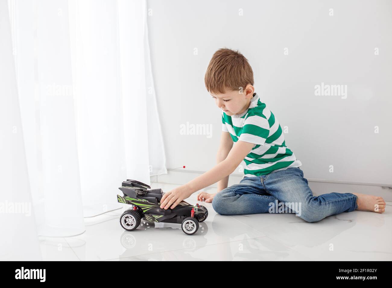 Ein Teenager in einem gestreiften T-Shirt spielt mit einem Spielzeugauto in einem hellen Raum. Stockfoto