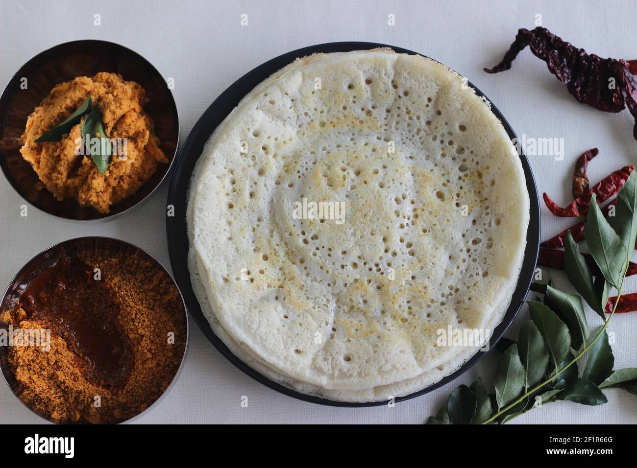 Indische Pfannkuchen werden auch als Dosa mit einem fermentierten Teig aus Reis und Linsen gemacht bekannt. Serviert mit idli podi chutney, sambar, Coconut Chutney und einem Glas Stockfoto