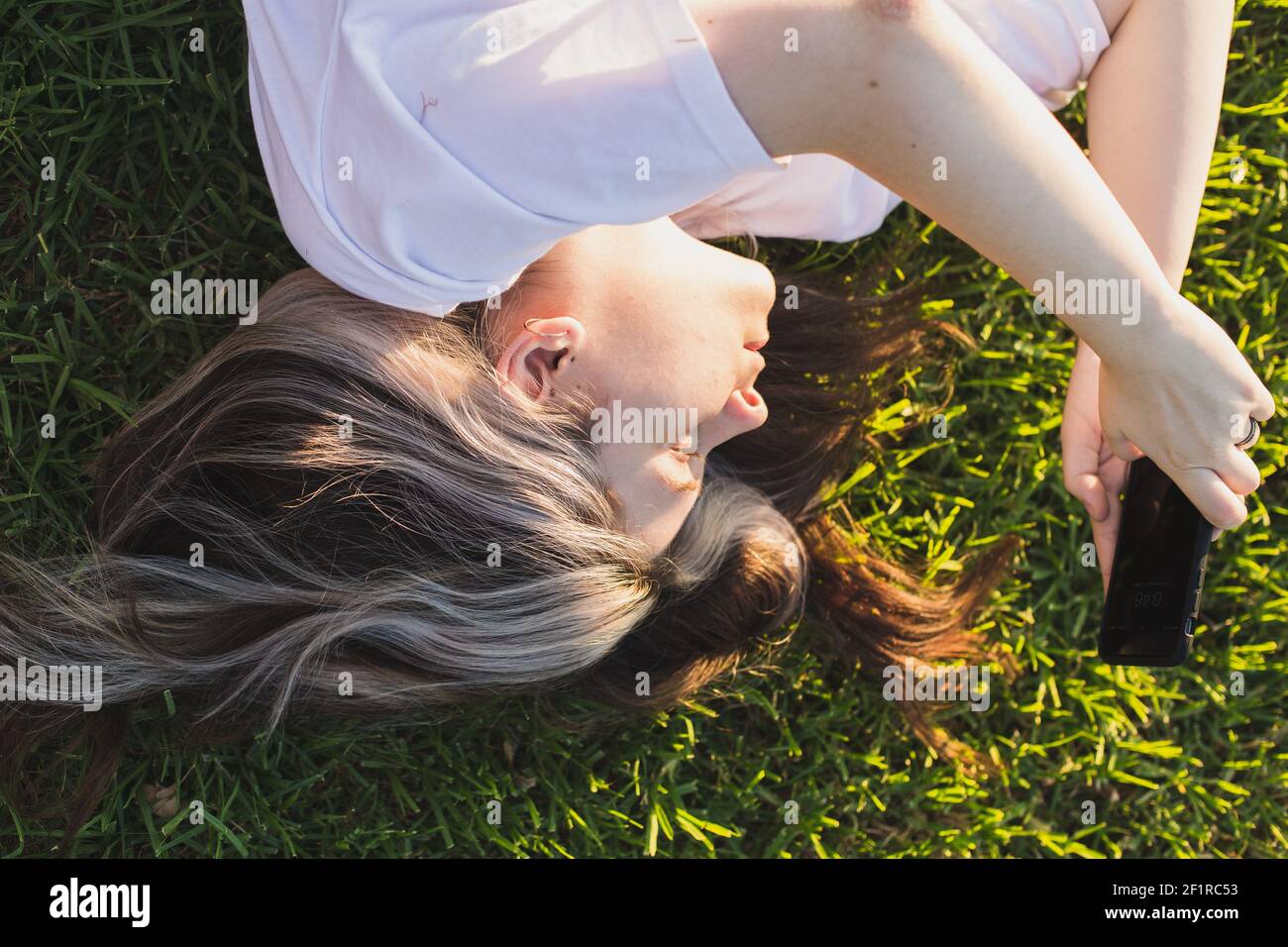 Porträt eines Mädchens auf Gras liegend mit einem Telefon in Ihre Hände bei Sonnenuntergang Stockfoto