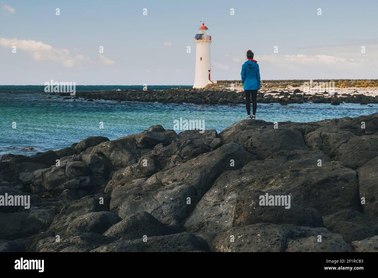 Junge Frau, die in der Ferne einen Leuchtturm auf der felsigen Küste sieht, Port Fairy, Australien. Stockfoto