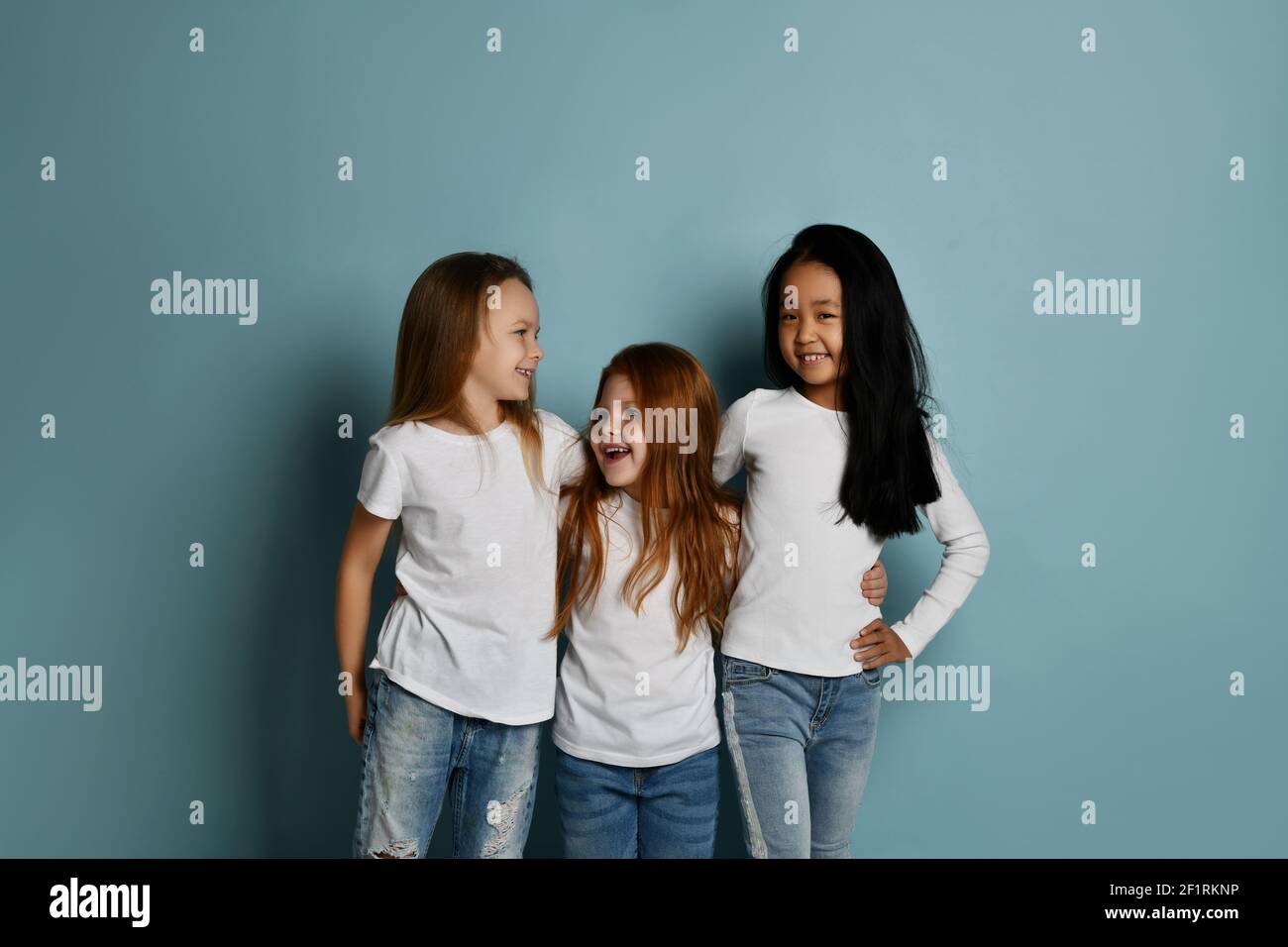 Gemischtes Rennen international glücklich Kinder Mädchen Freunde in Jeans und Weiße T-Shirts gehen zusammen umarmend lachend Stockfoto