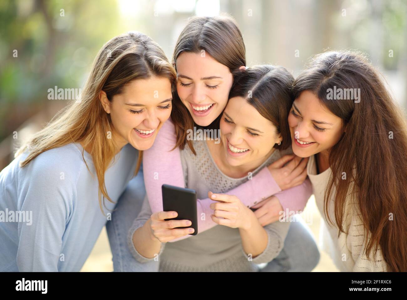 Vier glückliche Frauen überprüfen Smartphone-Inhalte scherzen in der Straße Stockfoto