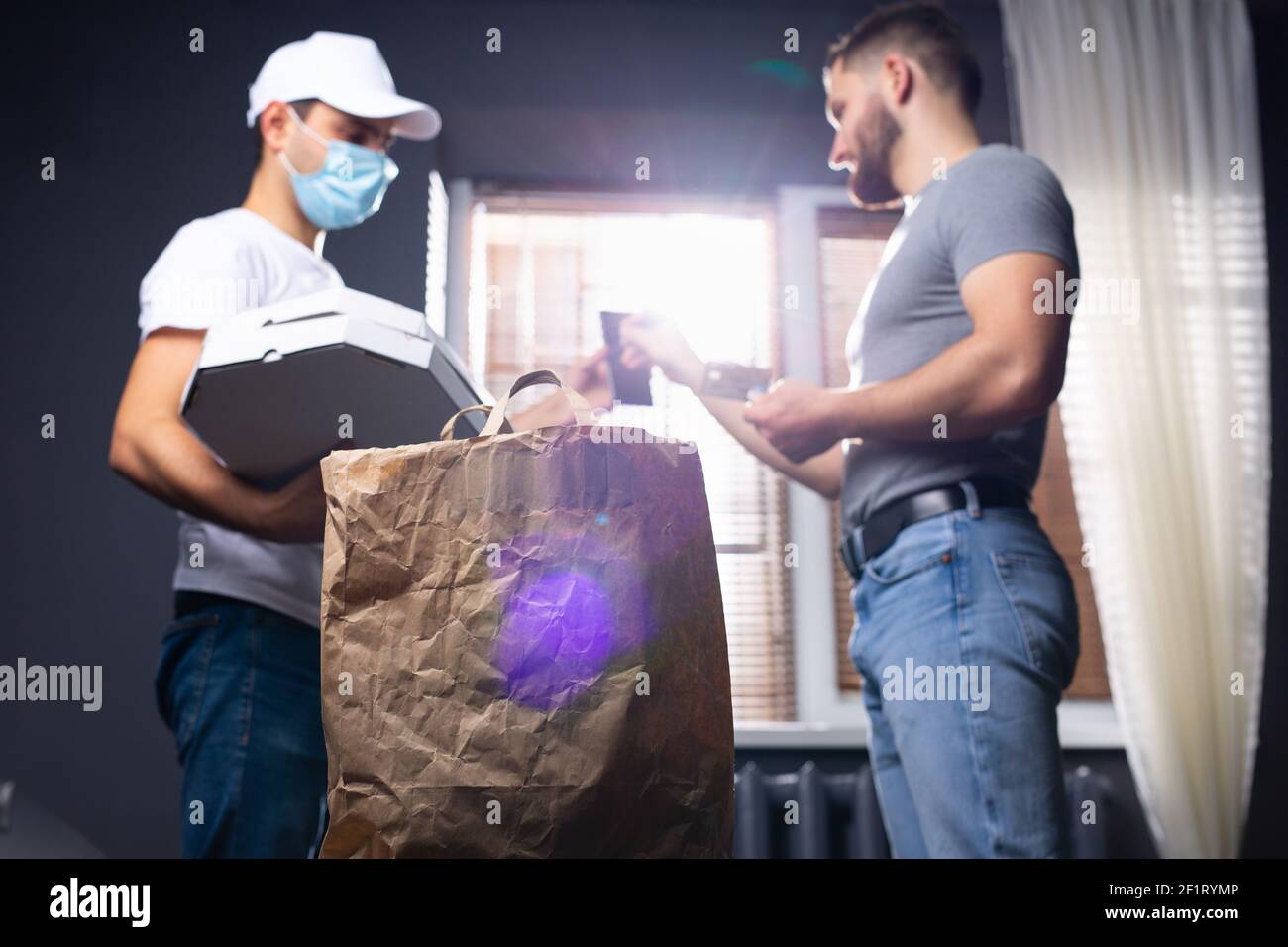 Während der Pandemie lieferte ein Kurier Lebensmittel nach Hause. Ein junger Mann wird mit einer Bankkarte belastet. Stockfoto