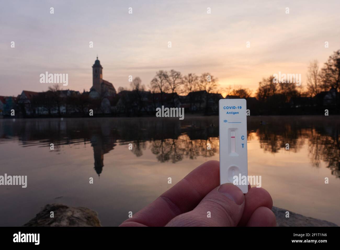 Negative covid-19 Testkassette in den Fingern. Kirche Reflexionen im Fluss in der Morgensonne. Deutschland, Nurtingen, Neckar. Stockfoto