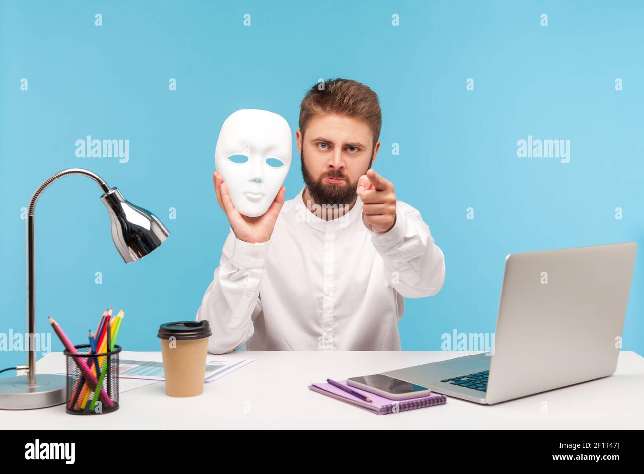 Serious bärtigen Mann Büroarbeiter hält weiße Gesichtsmaske und zeigt Finger auf die Kamera, beschuldigen Sie für das Verstecken Identität, Doppelzüngigkeit. Studio-Sho Stockfoto