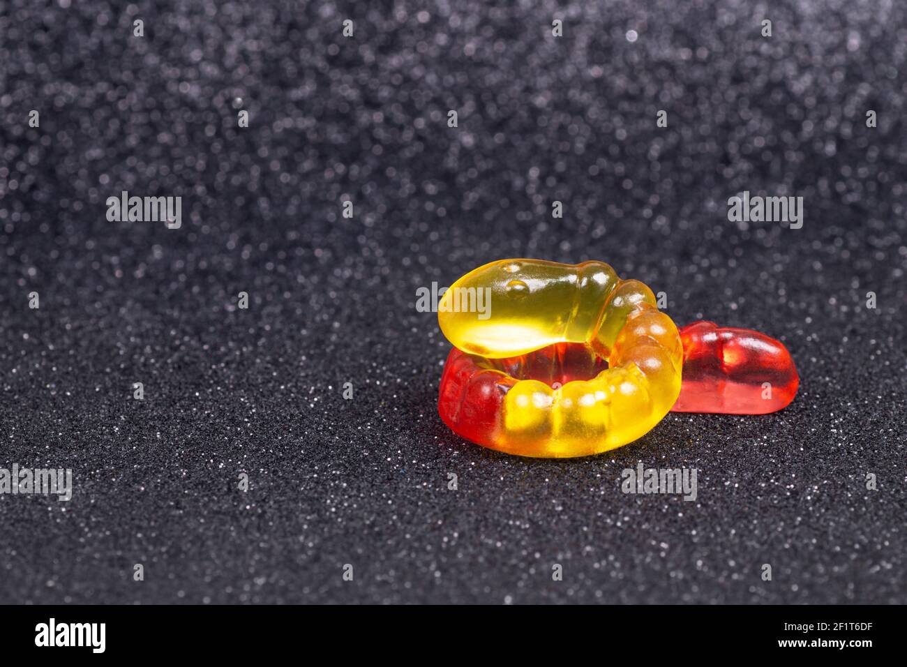 Nahaufnahme eines gewellten gelb-roten Gummiwurms auf dunklem Hintergrund mit hellem Bokeh-Effekt. Stockfoto