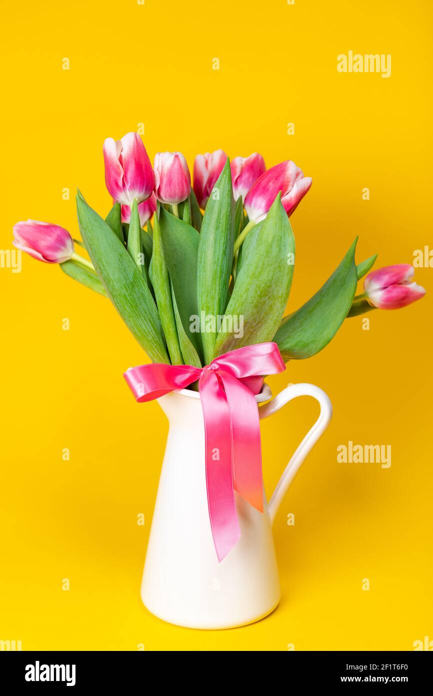 Nahaufnahme eines weißen Porzellantopfes aus blühendem Rosa Tulpen vor einem durchgehenden gelben Hintergrund Stockfoto