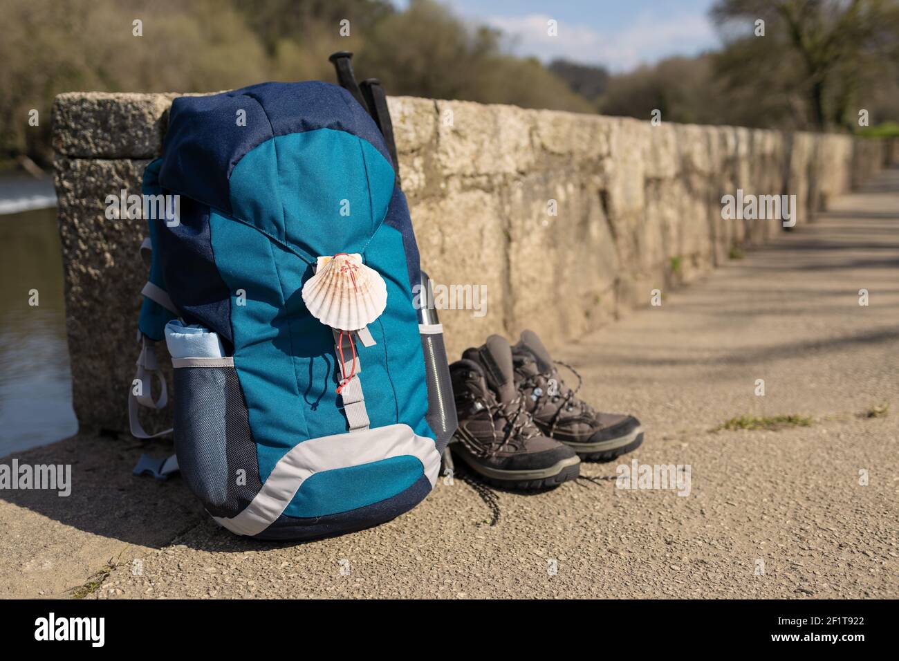 Rucksack mit Muschelsymbol des Camino de Santiago, Trekkingstiefeln und Stöcken, die an einer Steinwand angelehnt sind. Pilgerfahrt nach Santiago de Compostela. Speicherplatz kopieren Stockfoto