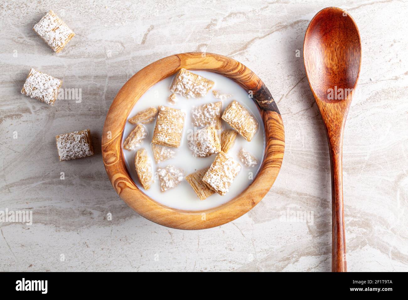 Ein einfaches Frühstückskonzept mit einer Schüssel mit Milchkorngetreide in Milchgröße auf einer Küchenarbeitspe aus Marmor. Ein Holzlöffel ist da, um zu essen. Stockfoto