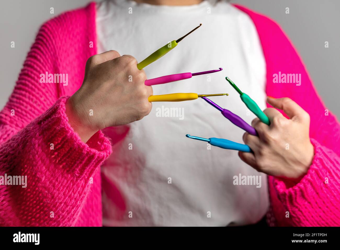 Frau mit einer neonrosa Strickjacke mit bunten Häkeln Nadeln in verschiedenen Größen Stockfoto
