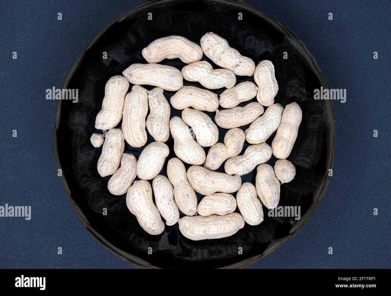 Samen von roten Erdnüssen in einer schwarzen Platte Nahaufnahme auf schwarzem Hintergrund. Stockfoto