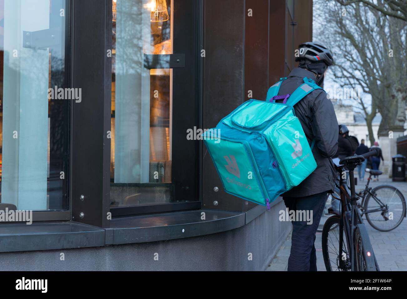 Deliveroo Rider mit Rucksack wartet in der Pick-up-Warteschlange Außerhalb des Restaurants für Speisen zum Mitnehmen nach Kundenwunsch Stockfoto