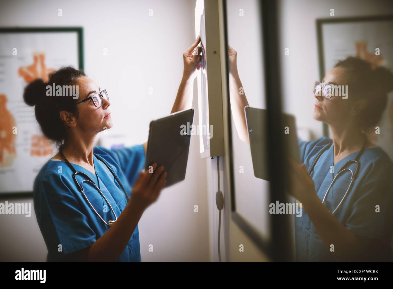 Seitenansicht einer lächelnden Krankenschwester mittleren Alters, die die Röntgenaufnahme in einer Arztpraxis überprüft. Stockfoto