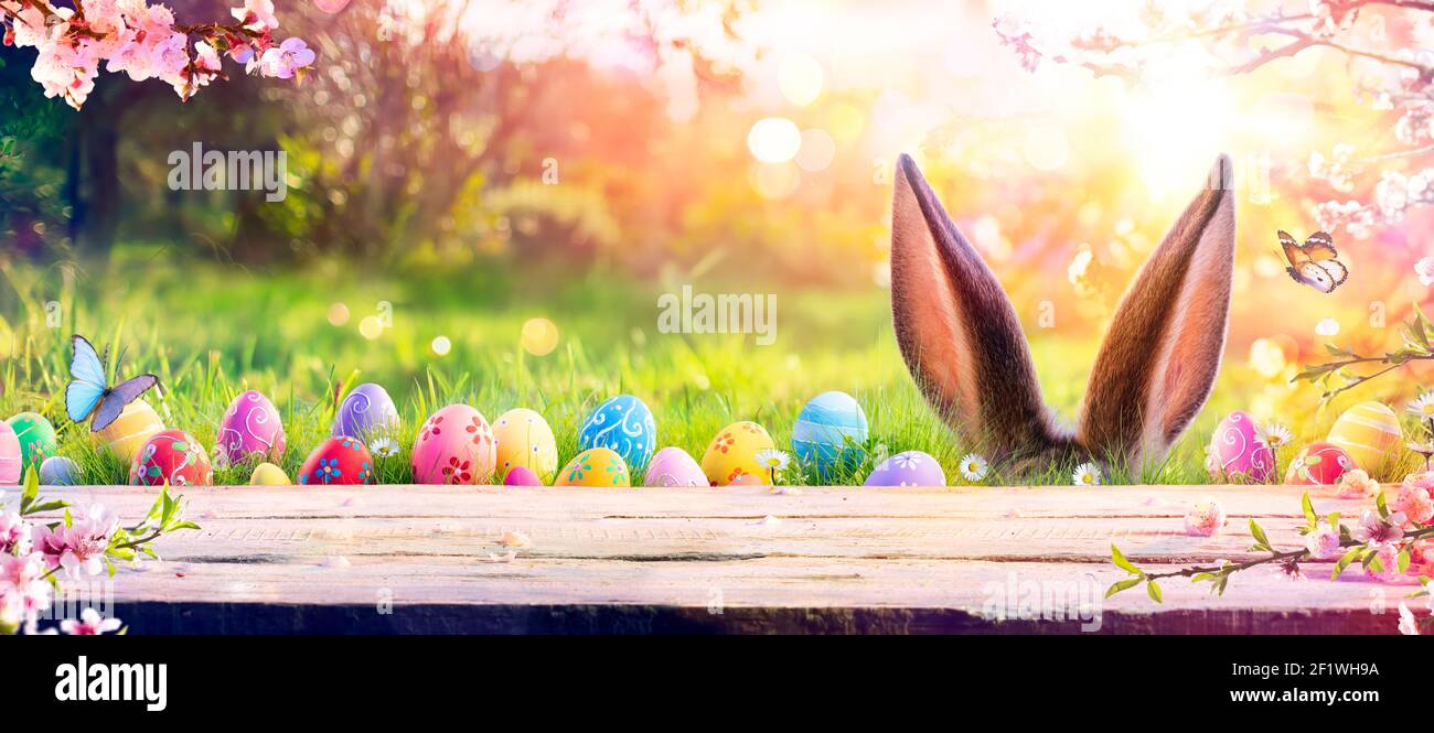 Abstrakt Defokussierten Ostertisch - Ohren Bunny Hinter Gras Und Dekorierte Eier In Blumigen Feld Stockfoto