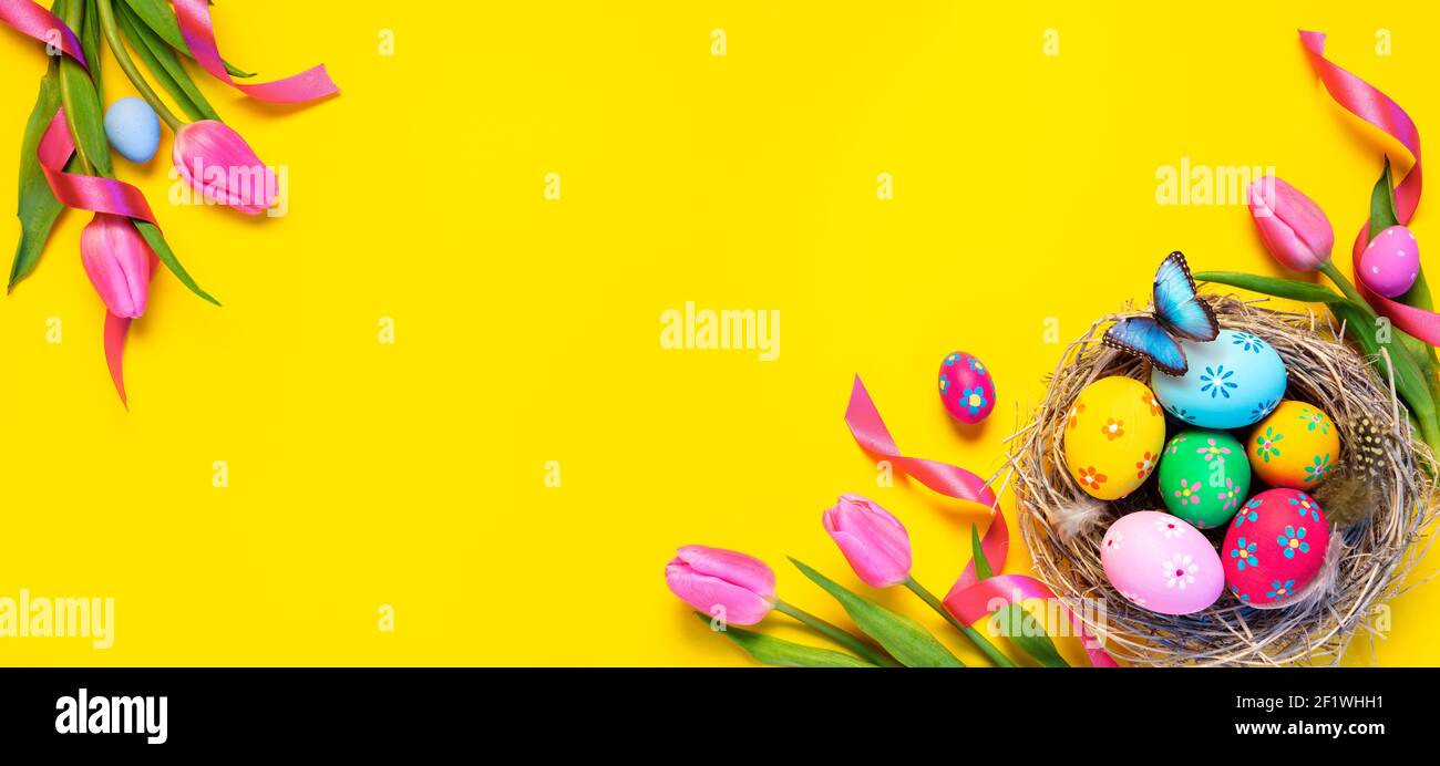 Ostern - Bunte Eier In Nest Mit Schmetterling Und Rosa Tulpen Auf Gelbem Hintergrund Stockfoto