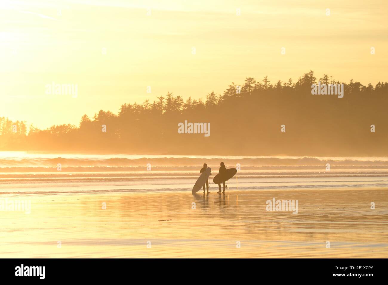 Zwei Surfer am Strand bei Sonnenuntergang. Stockfoto