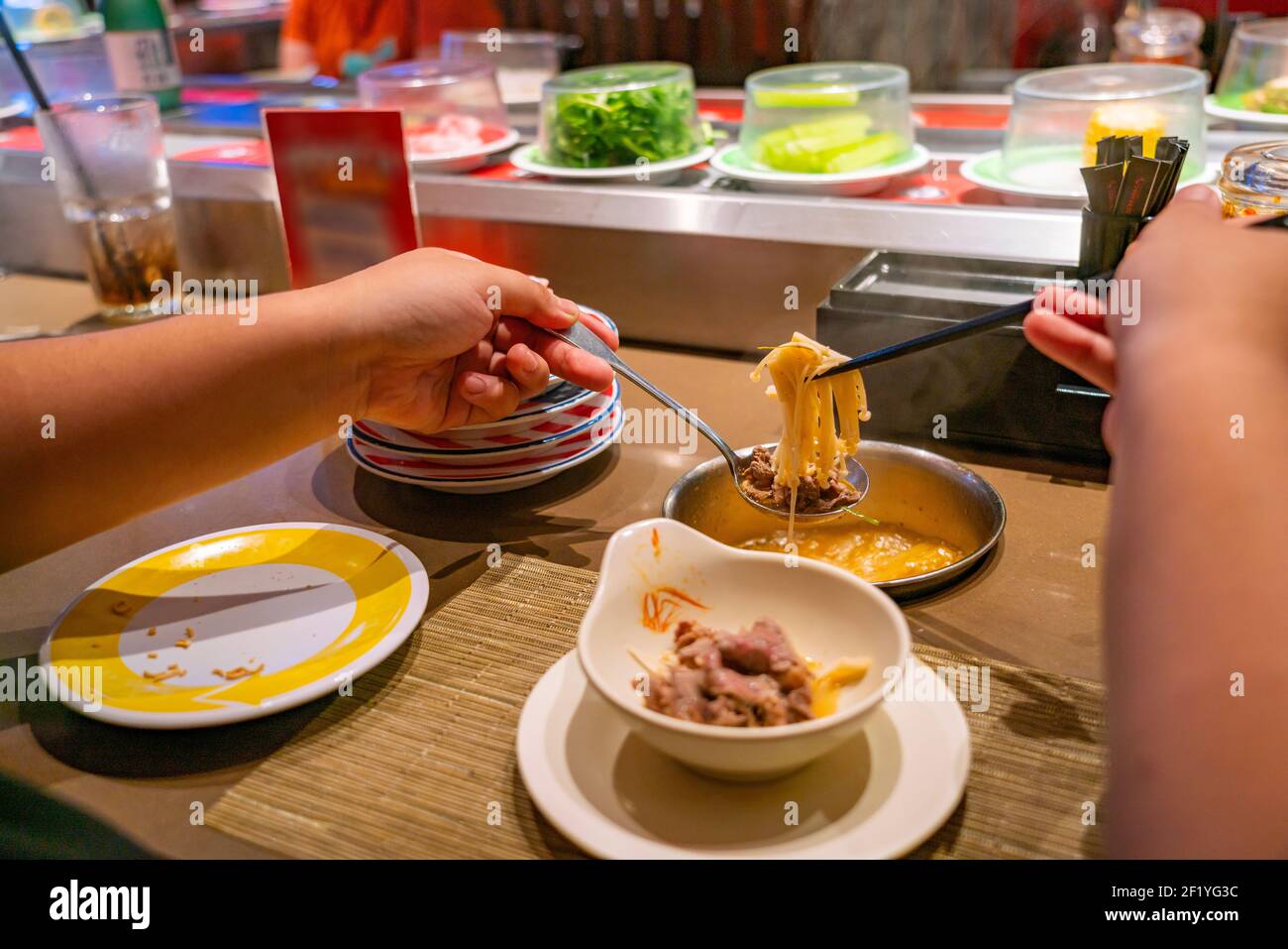 Asiatische Menschen essen Enoki Pilz Hotpot von Essstäbchen am Förderer Belt Restaurant Stockfoto