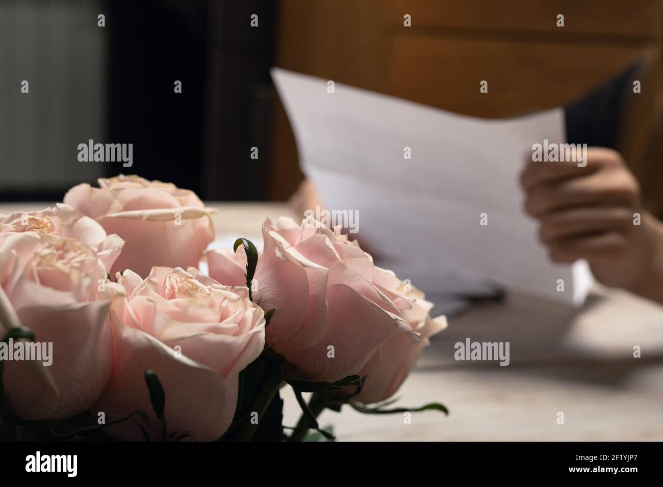 Papier Brief in menschlicher Hand Schuss mit Fokus auf rosa Rose Blume Knospe Bouquet. Handgeschriebene romantische Liebesbotschaft lesen. Korrespondenz, handschriftlich mich Stockfoto