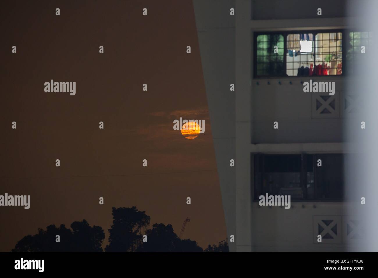 Riesiger orangefarbener Mond, der vom Horizont aufging, der Mond war neben einem Hochhaus-Häuserblock, 1. März 2021. Singapur. Stockfoto
