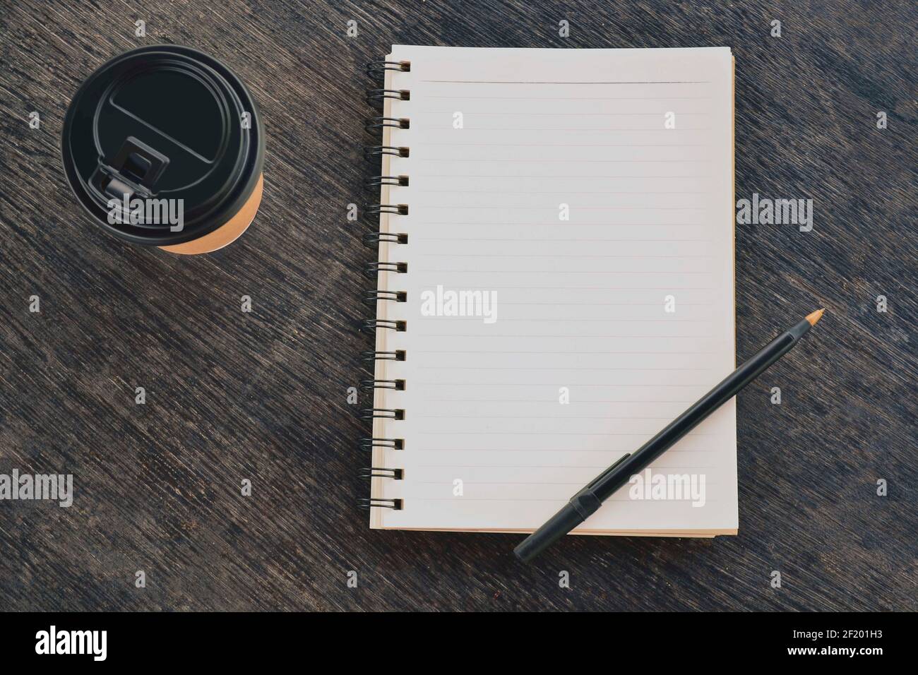 Notizblock mit Einweg-Kaffeetasse und Stift auf Holztisch Stockfoto