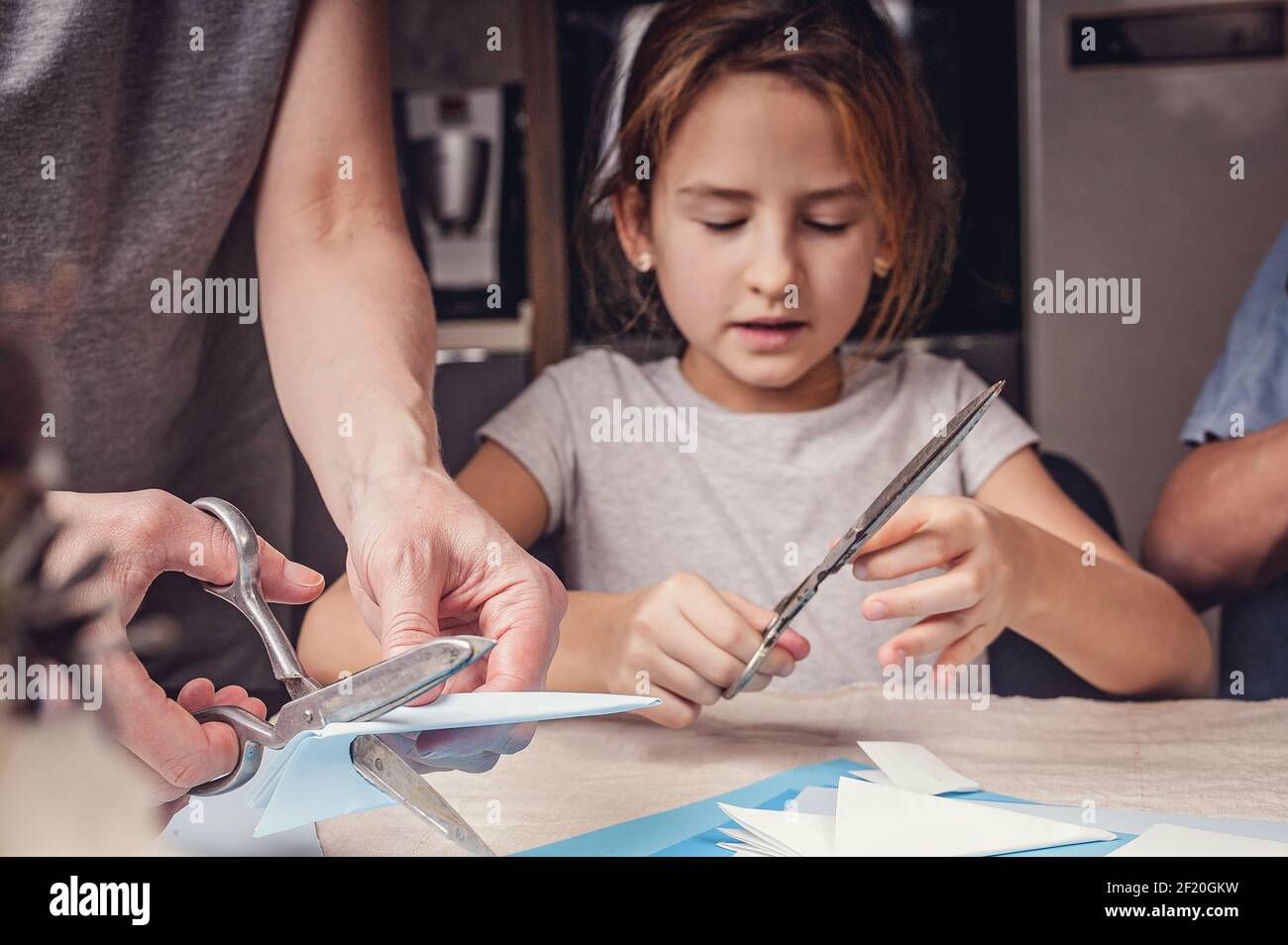 Kleine niedliche kaukasische Mädchen macht Papier Schneeflocken mit ihrer Mutter und Bruder. Urlaub, Winter Indoor-Aktivität, Lifestyle. Vorderansicht. Stockfoto