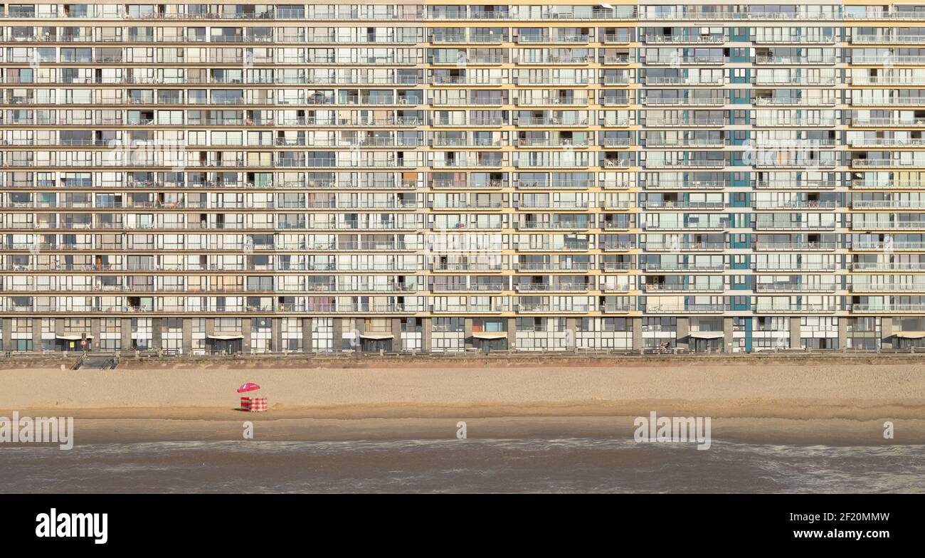Großes Appartementgebäude neben dem einsamen Strand von Ostende mit einem Windschutz und Sonnenschirm. Stockfoto
