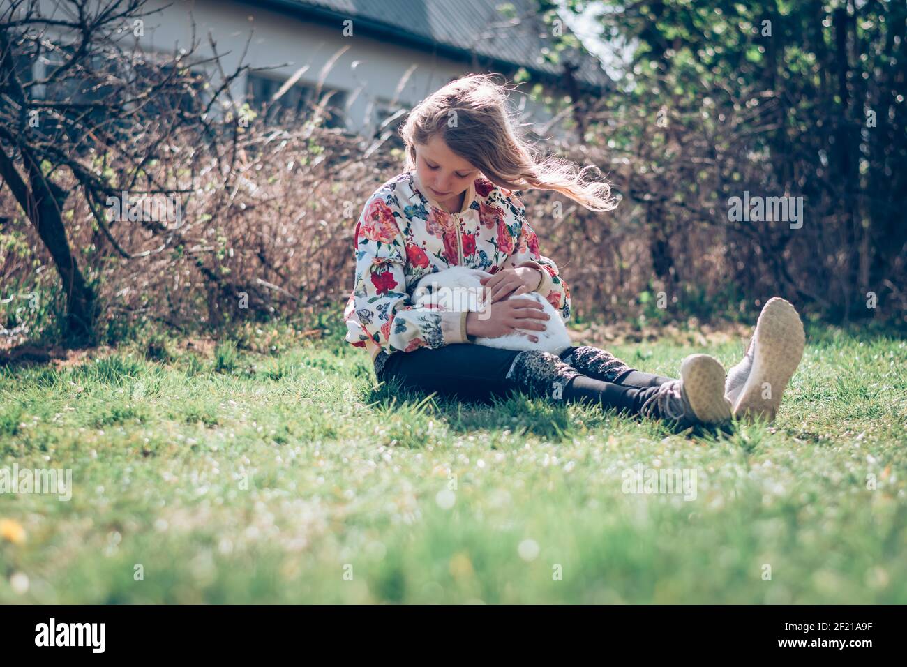 Kleines Mädchen, das im Gras sitzt und ein Weiß umarmt Flauschiges Kaninchen Haustier Stockfoto