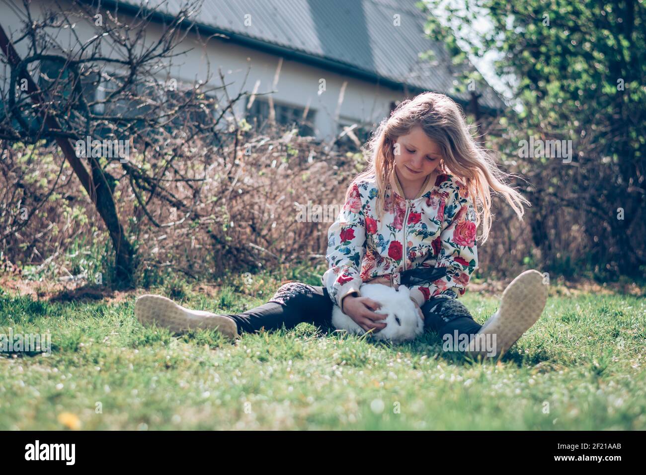 Kleines Mädchen, das im Gras sitzt und ein Weiß umarmt Flauschiges Kaninchen Haustier Stockfoto