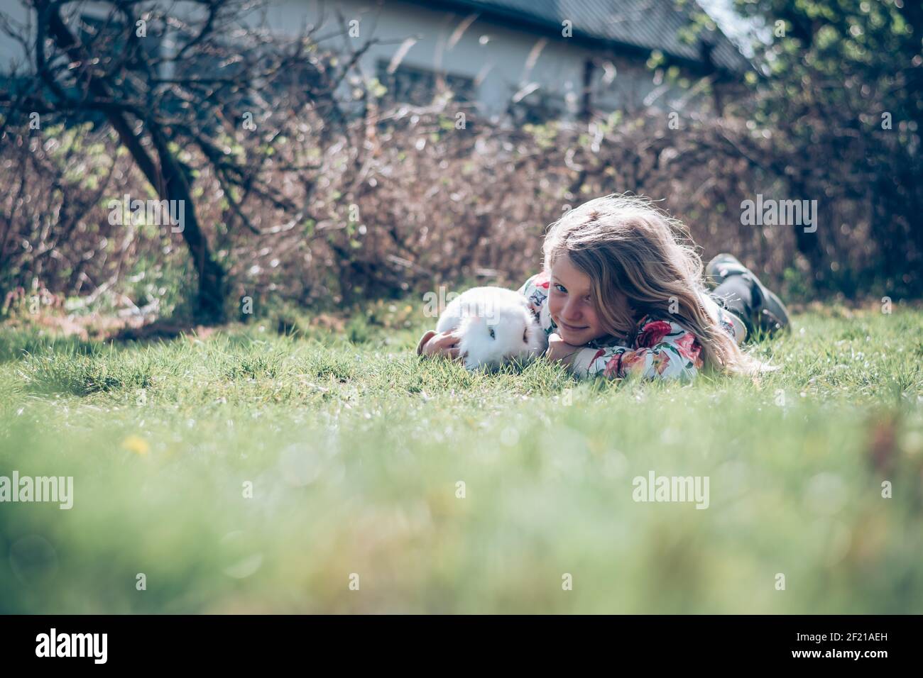 Kleines Mädchen mit weißem Kaninchen Haustier spielt im Garten Stockfoto