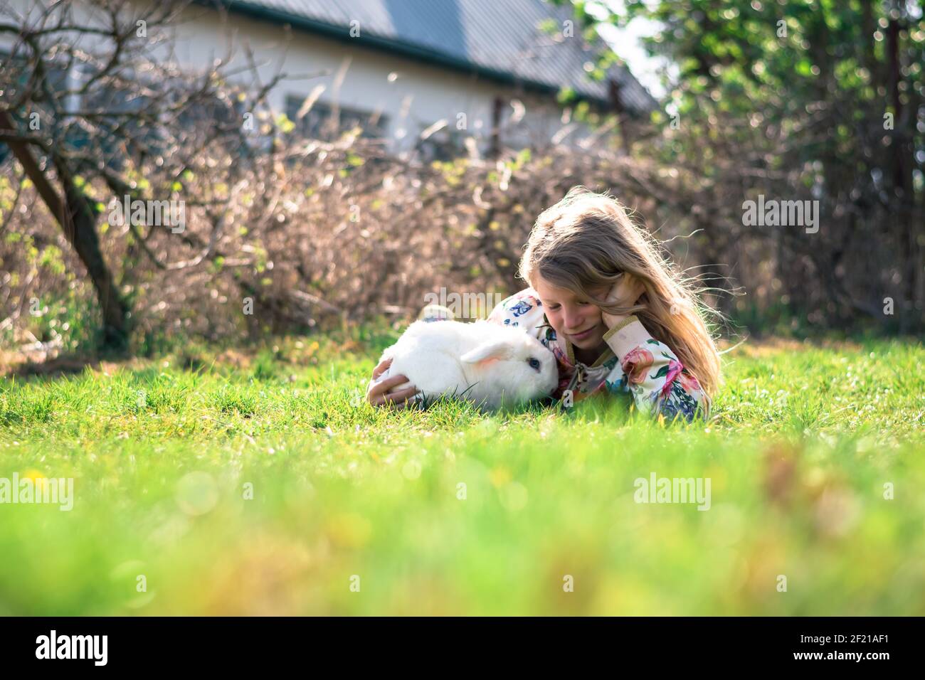 Kleines Mädchen mit weißem Kaninchen Haustier spielt im Garten Stockfoto