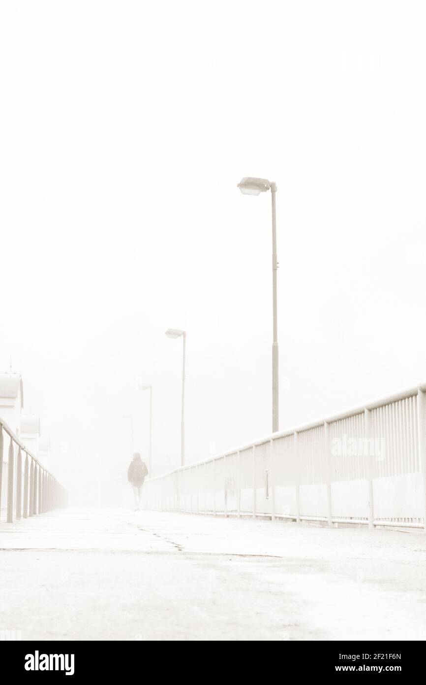 Geheimnisvolle Figur, die in einem nebligen Nebel entlang einer Brücke weggeht Tag Stockfoto