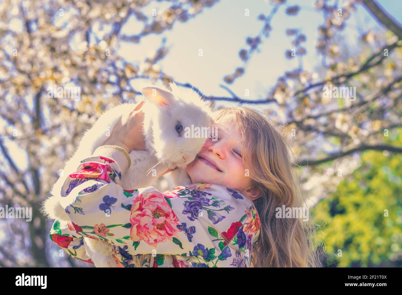 Liebenswert schöne Mädchen mit langen blonden Haaren umarmt weißen Ostern Kaninchen Tier in Magie bunten Frühling Natur unter Bäumen Stockfoto