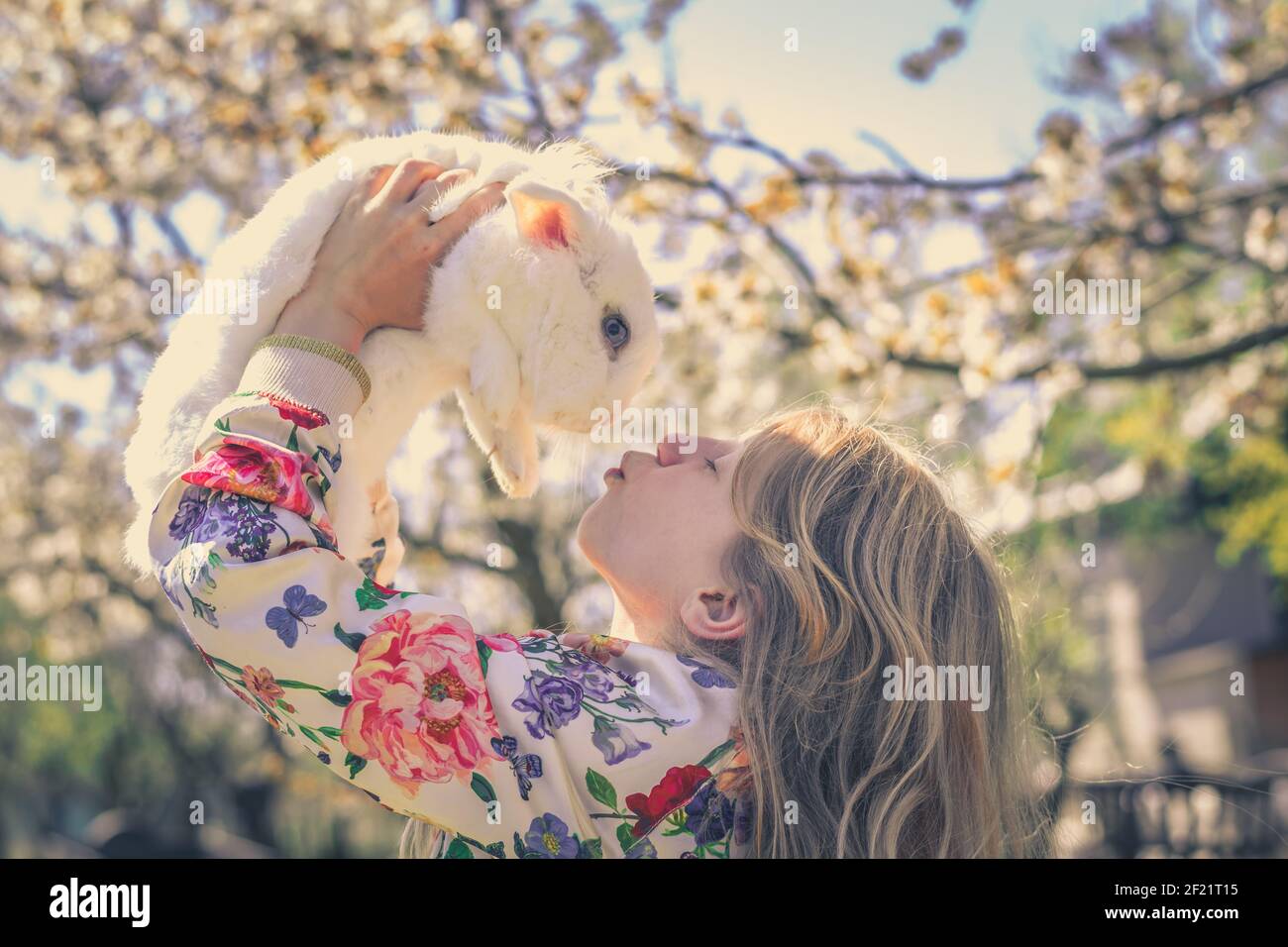 Liebenswert schöne Mädchen mit langen blonden Haaren umarmt weißen Ostern Kaninchen Tier in Magie bunten Frühling Natur unter Bäumen Stockfoto