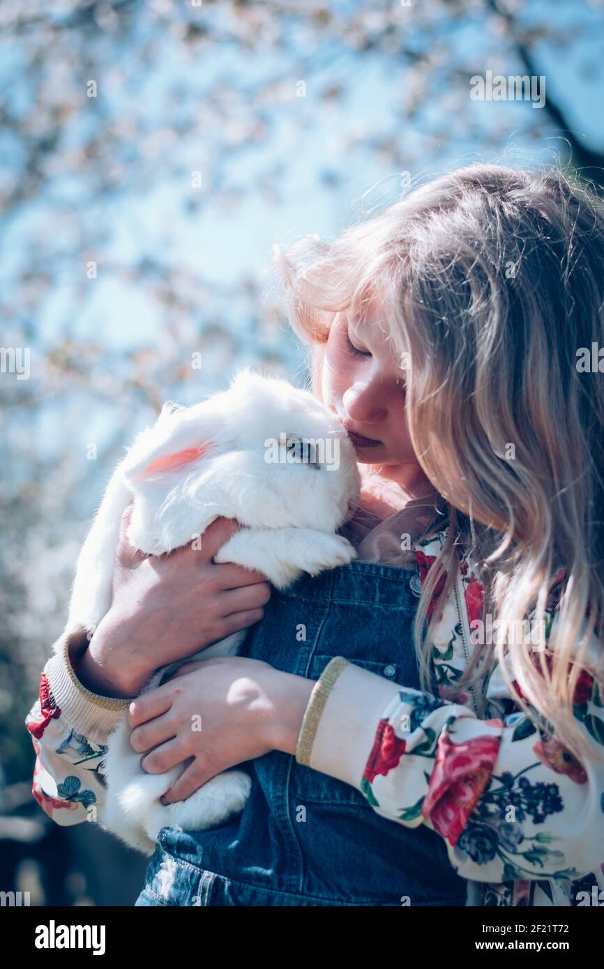 Liebenswert schöne Mädchen mit langen blonden Haaren umarmt weißen Ostern Kaninchentier Stockfoto
