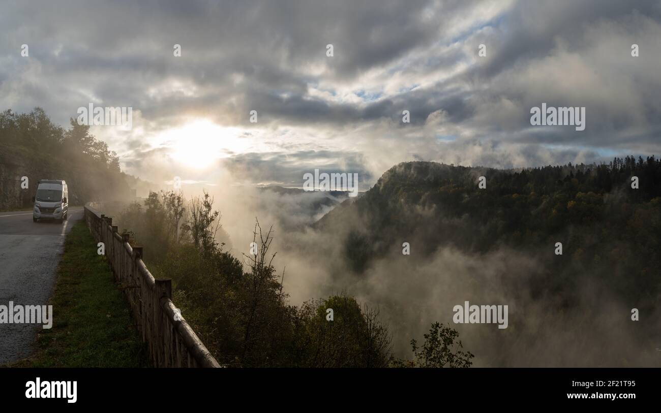 Ein geparkter Wohnmobil mit wunderschönen Herbstfarben Wald und Berglandschaft im Nebel und Nebel bei Sonnenbaden Stockfoto