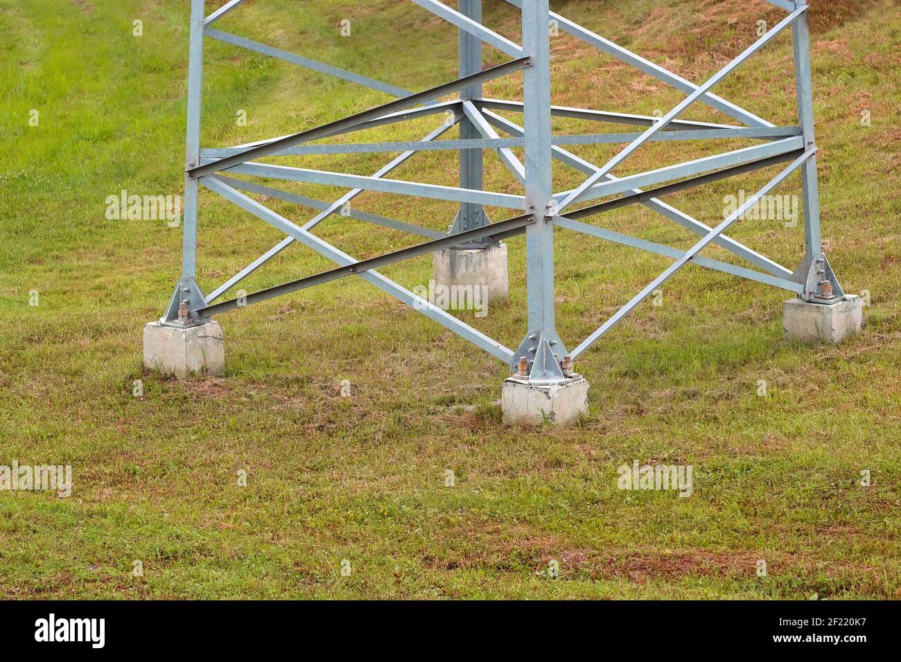 Unterer Teil einer großen elektrischen Stahlstütze auf einem Hintergrund von grünem Gras, Metallstruktur auf einem Betonsockel im Boden befestigt, Hochspannung A Stockfoto
