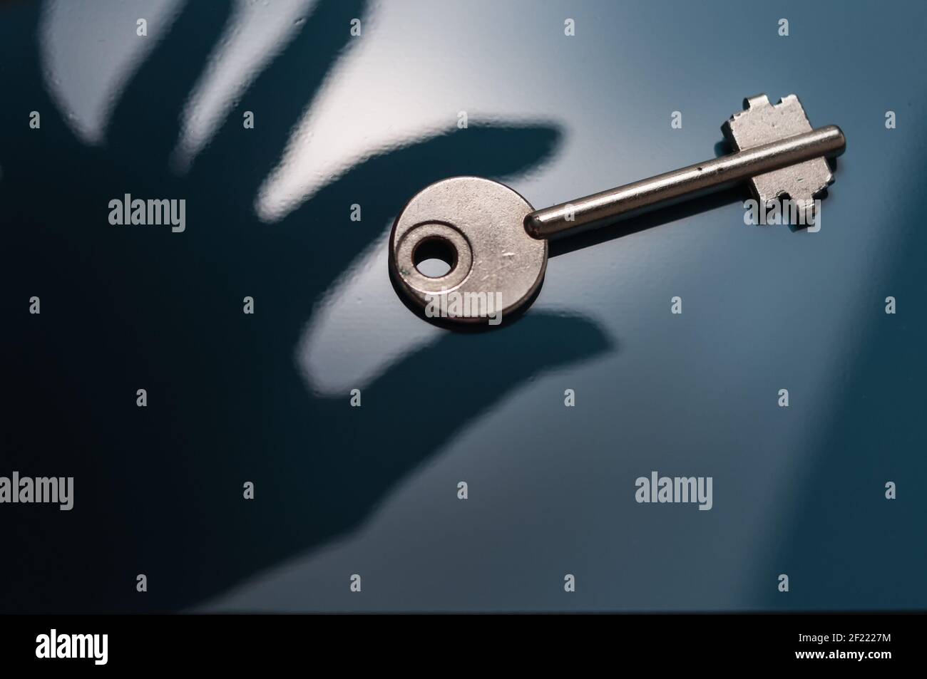 Shadow Play Safe Key wird von einer Schattenhand gegriffen Vor einem bläulichen Hintergrund Stockfoto