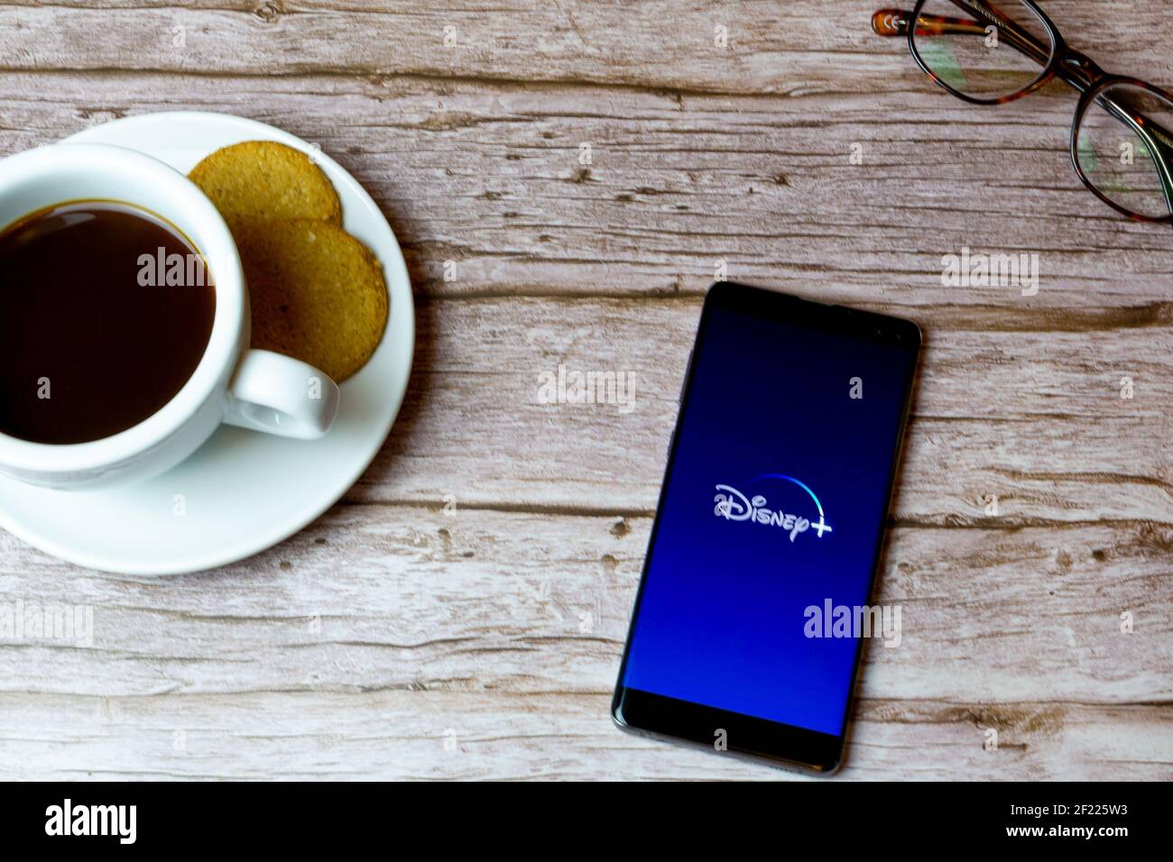 Ein Handy oder Handy auf einem Holz gelegt Tisch mit der disney plus App Öffnung auch einen Kaffee Und Brille Stockfoto