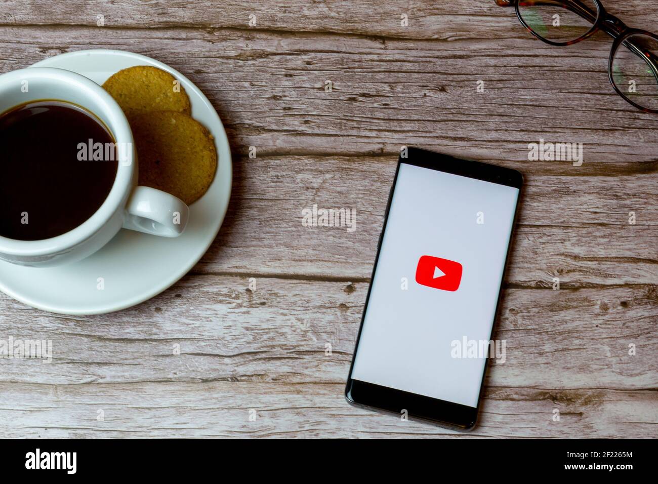 Ein Handy oder Handy auf einem Holz gelegt Tisch mit der Youtube App öffnen auch einen Kaffee und Brille Stockfoto