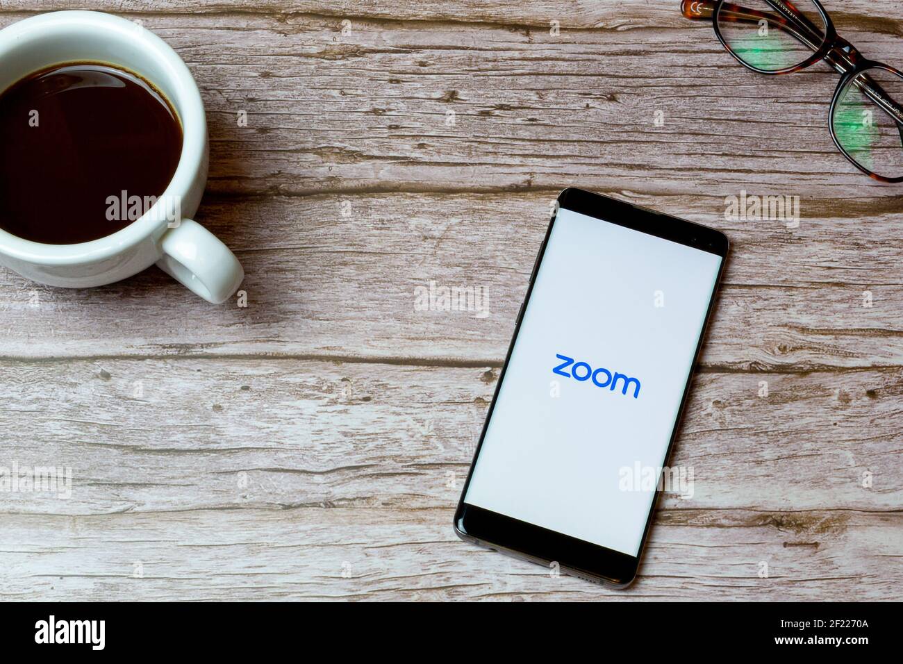 Ein Mobiltelefon oder Mobiltelefon auf einem Tisch Oder Schreibtisch mit der Zoom Calling App geöffnet und ein Kaffee daneben Stockfoto