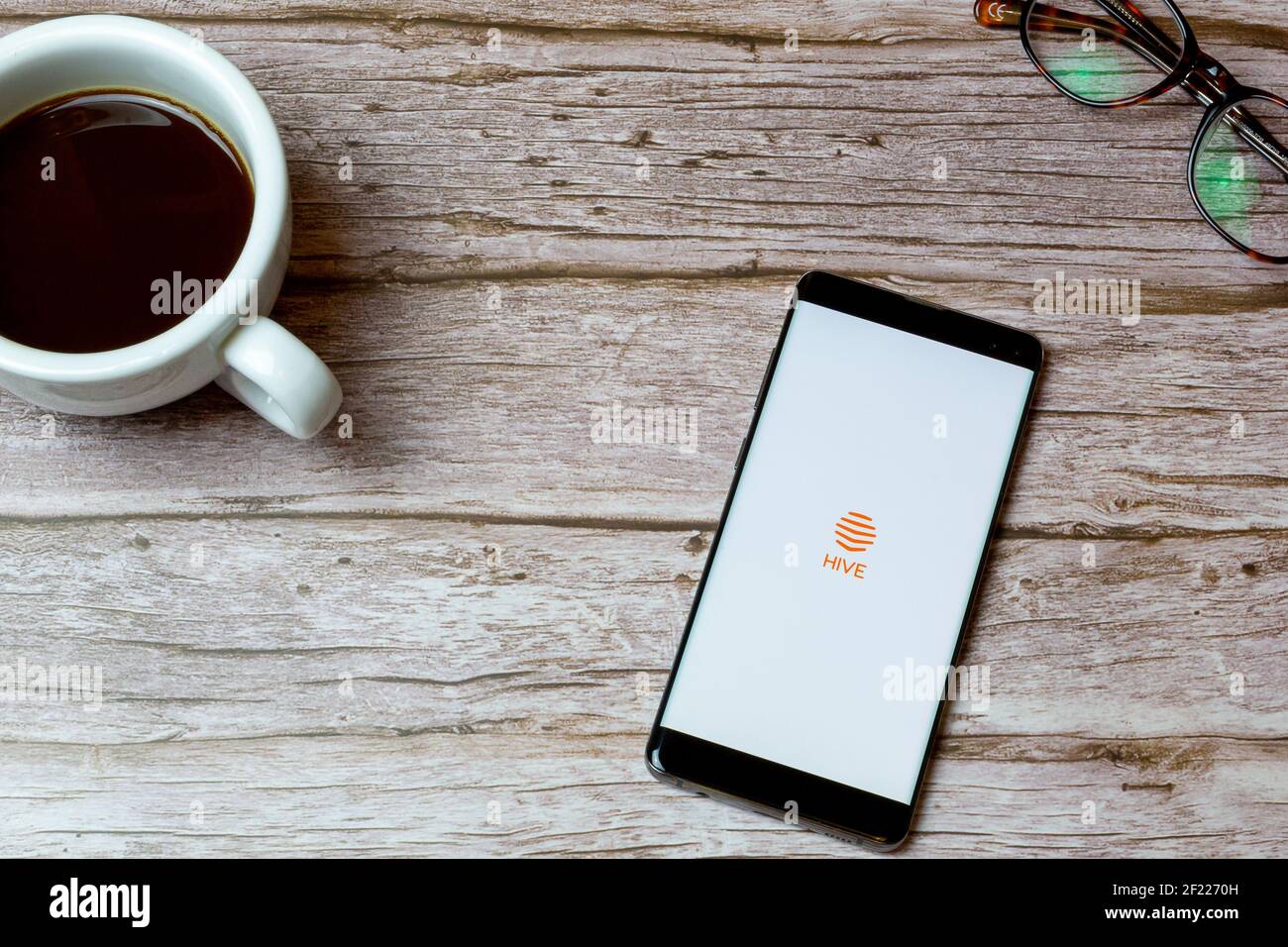 Ein Mobiltelefon oder Mobiltelefon auf einem Tisch Oder Schreibtisch mit der Hive Energy App geöffnet und ein Kaffee daneben Stockfoto