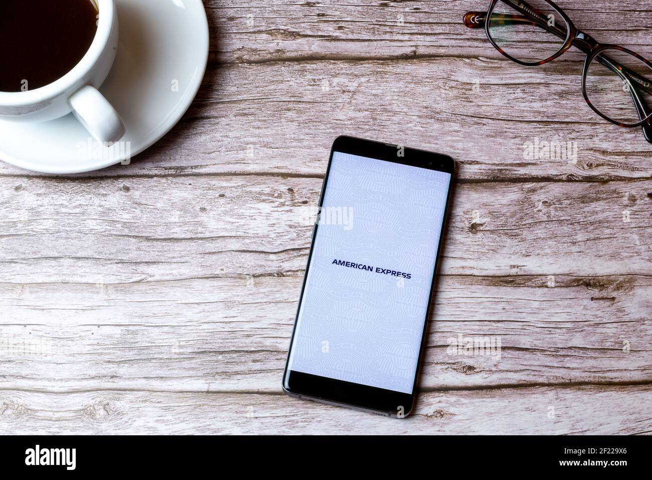 Ein Handy oder Handy auf einem Holz gelegt Tabelle mit der geöffneten American Express App neben einem Kaffee und Glas Stockfoto